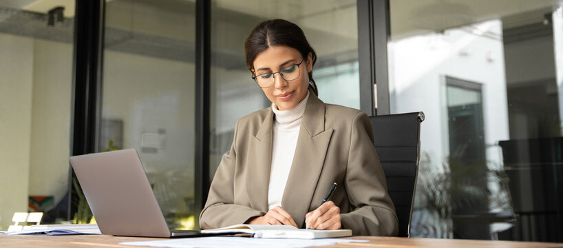 Professional financial specialist business lady working concentrated on laptop pc in office. Middle eastern woman using computer for work online, writing notes, watching webinar. Banner, copy space - Powered by Adobe