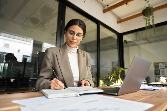 Focused professional latin hispanic financial specialist business lady working concentrated on laptop pc in office. Middle eastern woman using computer for work online, writing notes, watching webinar