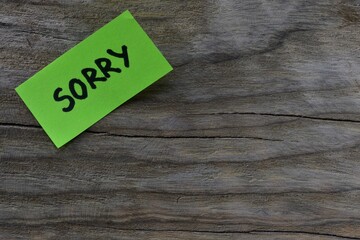 Message sorry on green sticky note on wooden board textured background. Black marker wrote word...