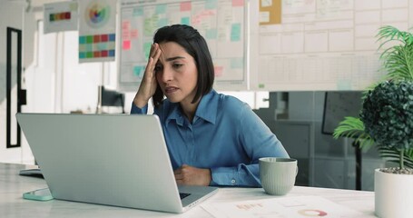 Young Brazilian woman reading unpleasant e-mail, feels frustrated due to stock market changes, inflation news, or financial reports affecting business or investments, demotion, downsizing, bankruptcy - Powered by Adobe