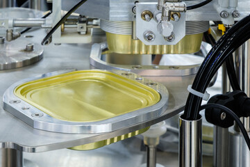 A machine is making a can of food. The can is yellow and silver. The machine is very precise and...