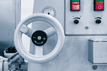 A silver machine with a silver wheel and a red button. The wheel is black and has a smiley face on it