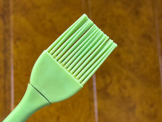 Close-up of a green silicone brush with evenly spaced bristles. The background has a warm brown color, creating a contrast with the bright green of the brush