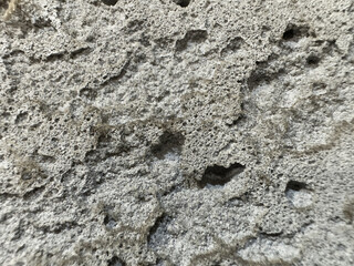 Close-up of a porous texture resembling volcanic rock. The surface is uneven, with numerous holes and indentations creating an interesting visual effect