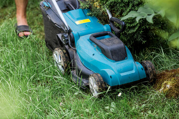 A man with a lawn mower mows the grass in the backyard. Agricultural machinery for garden maintenance. The banner.