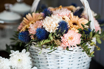 A beautiful, delicate bouquet of flowers in a white wicker basket in the interior. Close-up. Decoration.