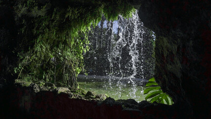 A cave opening frames a waterfall cascading into a pool of water, creating a secluded and...