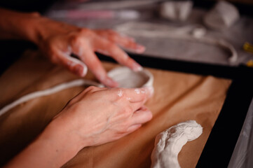 Close-up of hands carefully molding clay into a shape on a table. The image highlights the artistic...