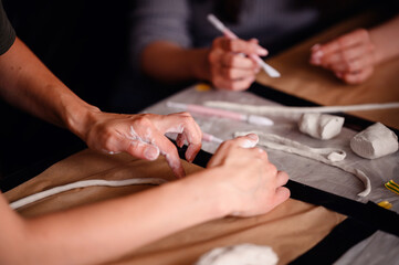 Close-up of hands using sculpting tools and shaping clay on a table. The image showcases the...