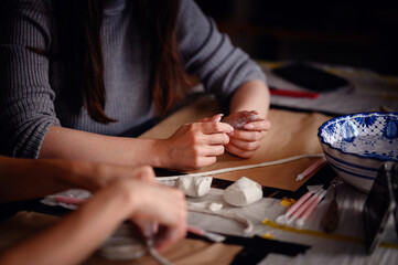 Close-up of hands using sculpting tools and shaping clay on a table. The image showcases the...