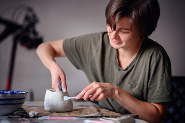 Two women working together on a clay pottery project, focusing on shaping and detailing the piece....
