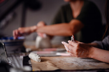Close-up of hands using a sculpting tool to add fine details to a clay pottery piece. The image...