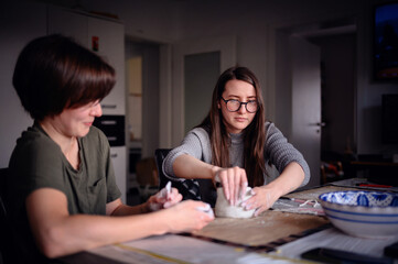 Two women engaged in a clay sculpting project, conversing and sharing a creative moment. The image...