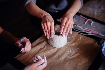 Close-up of hands carefully shaping a clay pottery piece on a crafting table. The image emphasizes the tactile and creative aspects of pottery making.