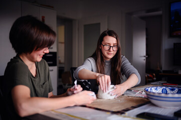 Fototapeta premium Two women engaged in a clay sculpting project, conversing and sharing a creative moment. The image captures collaboration and artistic expression in a relaxed setting.