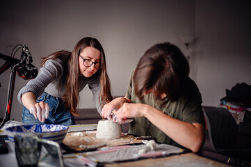 Two women working together on a clay pottery project, focusing on shaping and detailing the piece....