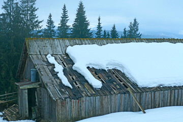 Snow lies on the roof of a wooden house. Winter in a mountain village