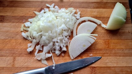 Chopped onions and a knife lie on a wooden cutting board