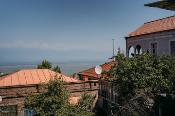 Panoramic view of Sighnaghi, Georgia, a historic town with red rooftops and lush green hills, overlooking the Alazani Valley on a clear summer day