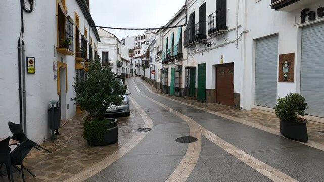 Gaucin, Spain - January 26, 2025 - A quiet, narrow street in a small Spanish town with wet pavement, white buildings, colorful shutters, balconies, and potted plants.
