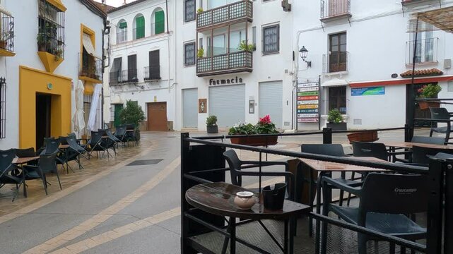 Gaucin, Spain - January 26, 2025 -A small town square with outdoor caf&eacute; seating, white buildings, flower pots, and closed shop fronts, after rain, creating a calm atmosphere.