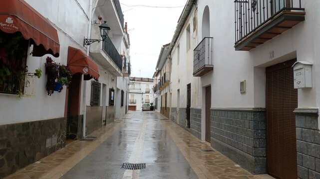 Gaucin, Spain - January 26, 2025 -A quiet narrow street in a Spanish village after rain, featuring white walls, flower pots, wrought iron balconies, and a peaceful atmosphere.