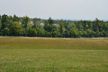 A scenic view from Cmrok, featuring a pathway lined with streetlights leading towards the city of Zagreb, with the distinctive domes of the Mirogoj cemetery arcades visible in the distance