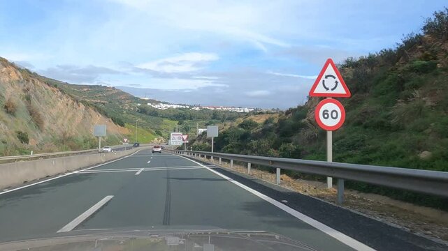 Sotogrande, Latvia - January 26, 2025 - A curving highway through hilly terrain with road signs and vehicles, under a partly cloudy sky. Scenic countryside drive.
