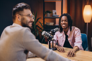 Two male podcasters smiling and talking during a recording session in a professional studio