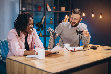 Male podcasters sharing jovial moment during recording session, professional studio microphones...