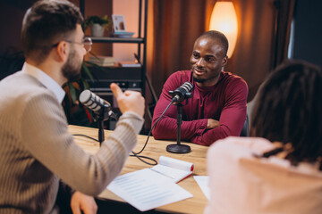Podcasters collaborating during live recording, speaking into microphones within sleek professional...