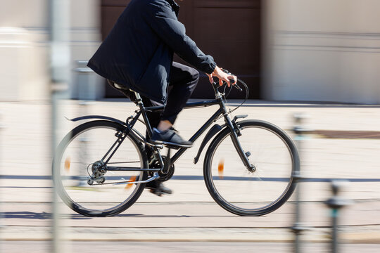 Man in dark jacket cycling black bicycle on European city street dynamic motion blurred background on sunny day. Urban bike commute work ride employee healthy lifestyle eco-friendly transport - Powered by Adobe