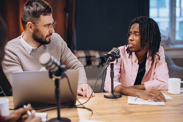 Podcasters collaborating, wearing headsets, speaking into condenser microphones near laptop while...