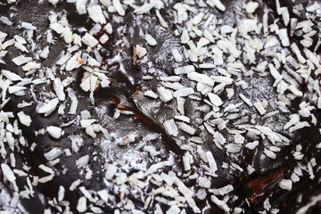 Chocolate glazed biscuit topped with coconut flakes. Smooth chocolate layer with a sprinkling of shredded coconut texture. Sweet treat for dessert or snack texture. Coconut chocolate background.