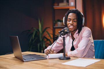 African American man content creator speaking into microphone, recording podcast in home studio...