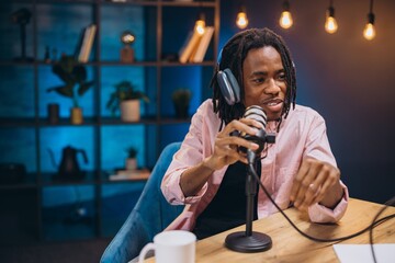 African American male content creator speaking at his microphone and recording a podcast episode in a modern studio