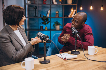 Podcasters engaging in lively conversation while recording an episode in a modern studio,...