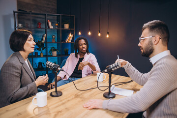 Podcasters interviewing a guest in a studio, discussing interesting topics and sharing their expertise with microphones