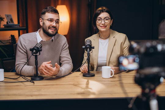 Podcasters recording video interview in professional studio, multiple microphones, camera capturing dynamic discussion between speakers