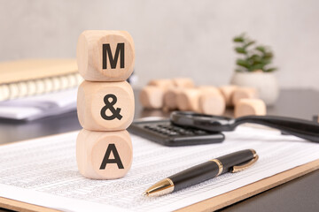 wooden blocks spelling MA stacked on financial documents, with office supplies