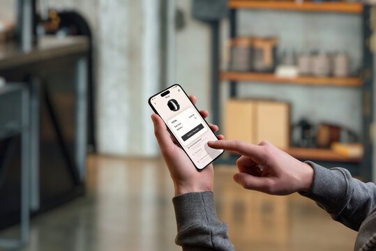 Hand confirming a smartwatch purchase on a smartphone via a modern eCommerce app. The setting is a cozy home environment