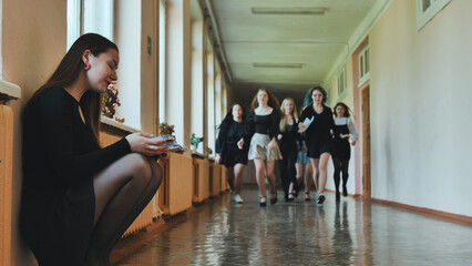 Capturing a moment of solitude, teenage student immersed in reading while classmates dash through school hallway