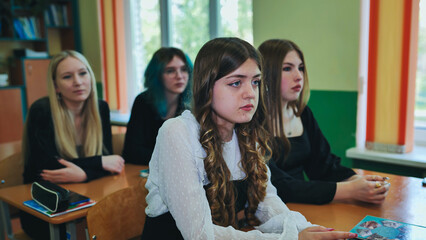 Four high school girls are sitting at desks in a classroom, listening to a lecture and participating in the school day