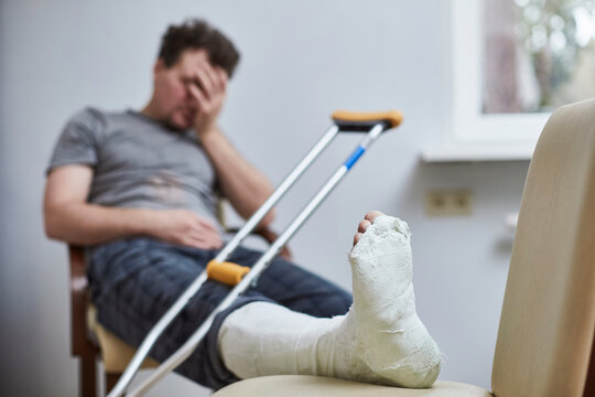 A sad man with a broken leg sits on a chair. Illness concept.