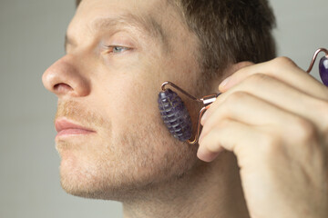 a man massages his face with a roller massager, skin care concept