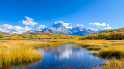 Fototapeta premium Snow-capped mountain peak reflects in a calm alpine lake surrounded by golden autumn foliage under a clear blue sky.