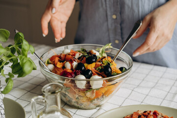 Women's hands cooking and mixing salad with tomato  olives mozzarella vegetables arugula dressing with balsamic vinegar and olive oil in a large bowl a healthy balanced meal 