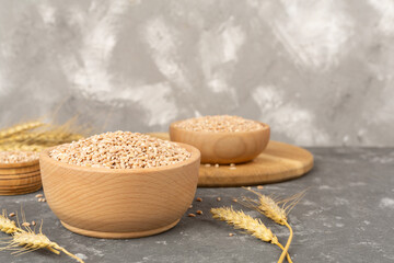 Bowl with spelt grain and ears on concrete background