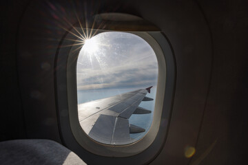 Naklejka premium View through the flying plane window on a beautiful blue skyscape, shining sun, and airplane wing. Travel time and transport concept.