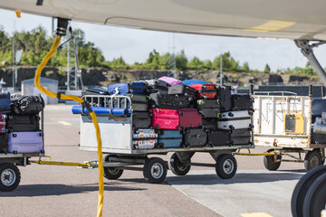 Airport luggage trolley with travel baggage loaded from the airplane, on the runway. Transport and...